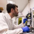 Calum Shelden wears PPR and works in a lab with a large microscope