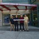 Two UC Davis ECE students and professors stand near a building with a red sign that says John D Kemper Hall of Engineering
